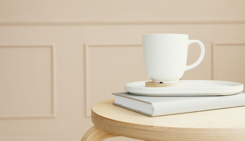 A white ceramic mug on a tray, placed over a closed book on a wooden table.